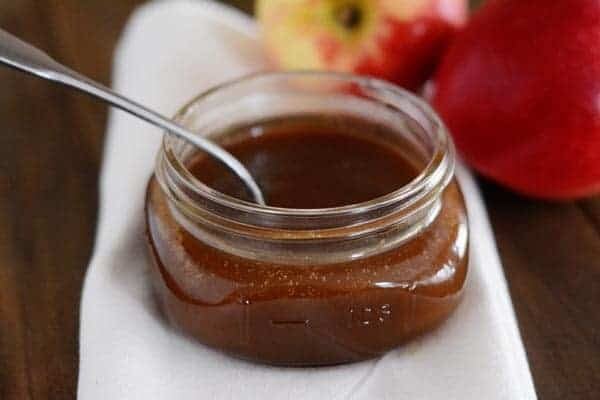A small mason jar of caramel sauce with a spoon inside. 