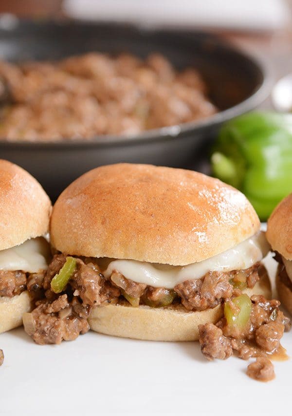 Philly cheesesteak sloppy joe's in front of a skillet of sloppy joe meat.