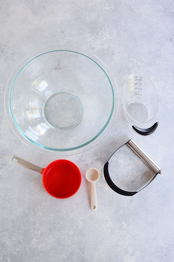 Top view of a glass bowl, red measuring cup, spoon, and liquid measuring cup. 