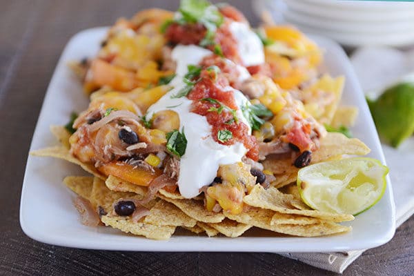 A white platter of cheesy fajita nachos topped with salsa and sour cream.