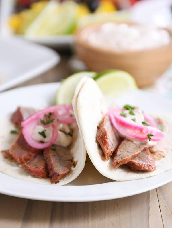 Steak fajitas in tortillas on white plate.