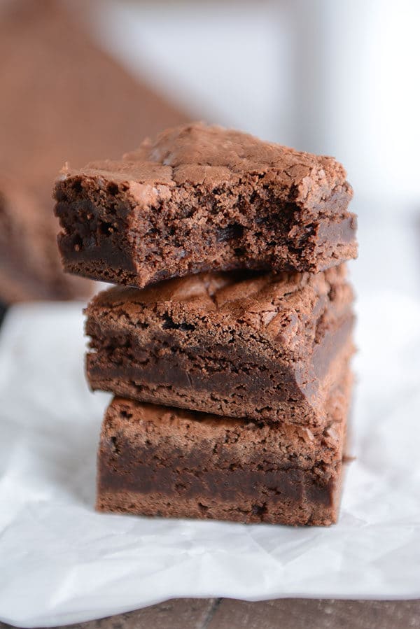 A stack of three brownies with a bite taken out of the top brownie.