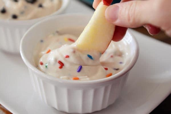 An apple slice being dipped in a ramekin of funfetti dip.