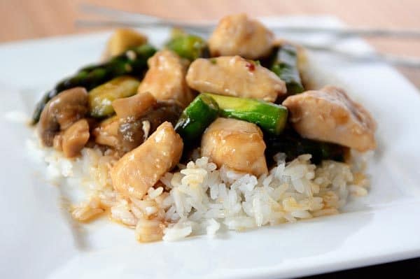 A plate full of cooked white rice topped with chicken and asparagus stir fry. 