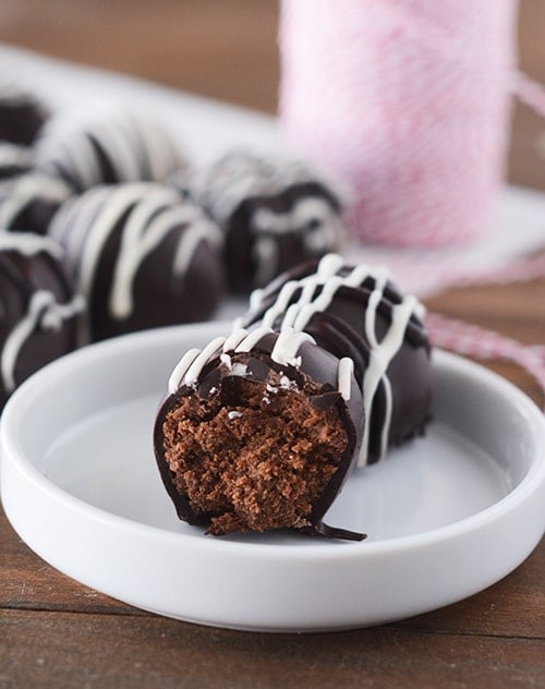 A white plate with a half eaten chocolate gingerbread truffle and a full truffle behind it.