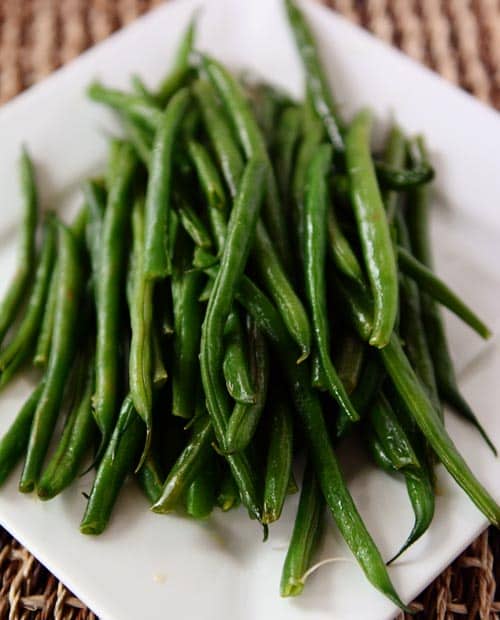 A white platter with a top view of fresh cooked green beans.