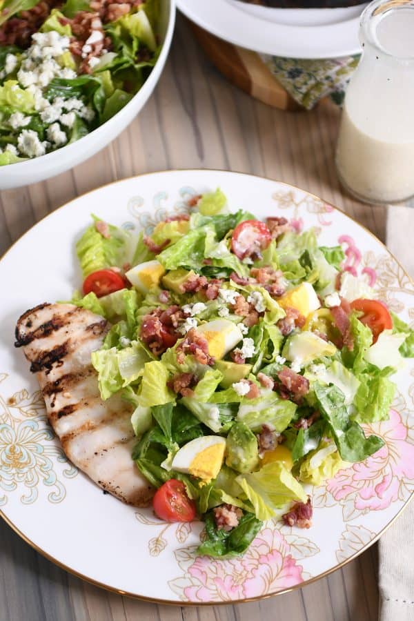 Grilled chicken cobb salad on white plate with pink flowers.