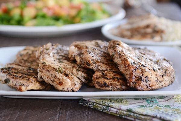 A white rectangular plate with four grilled chicken breasts side-by-side on the plate.