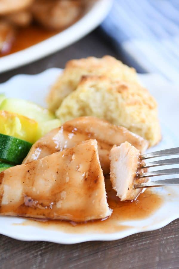 White plate with grilled sweet and sour chicken, zucchini and biscuits.