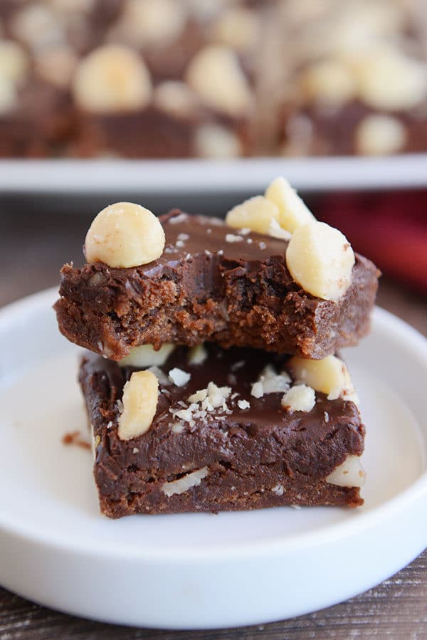 Two chocolate macadamia nut brownies stacked on top of each other with a bite taken out of the top one.