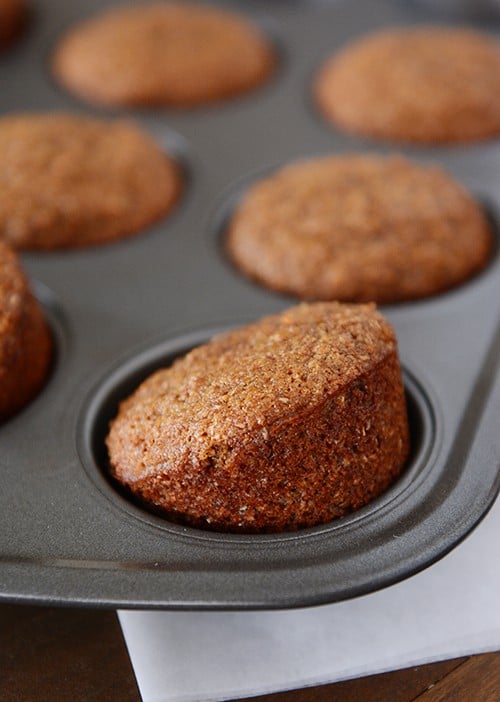 Golden brown muffins in a muffin tin with the front muffin slightly tipped up.