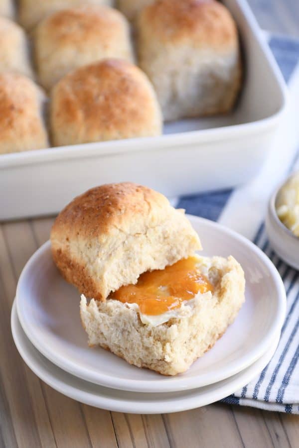 Fluffy honey oat dinner roll on white plate with butter and apricot jam.