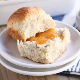 Fluffy honey oat dinner roll on white plate with butter and apricot jam.