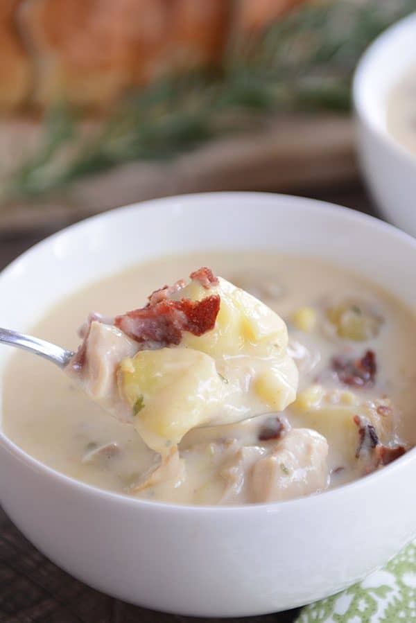 A bowl filled with potato soup, topped with crumbled bacon, with fresh sage and a loaf of bread in the background.