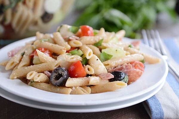 A white plate of Italian pasta with chopped olives and tomatoes.