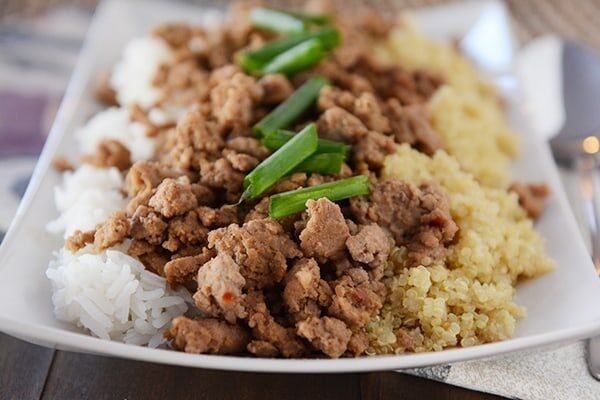 A white platter with half cooked white rice and half quinoa, topped with cooked beef.