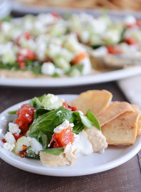 A white plate of greek hummus dip with crackers on the side. 