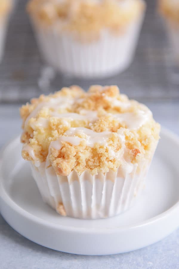 A streusel and frosting topped lemon muffin in a white liner.