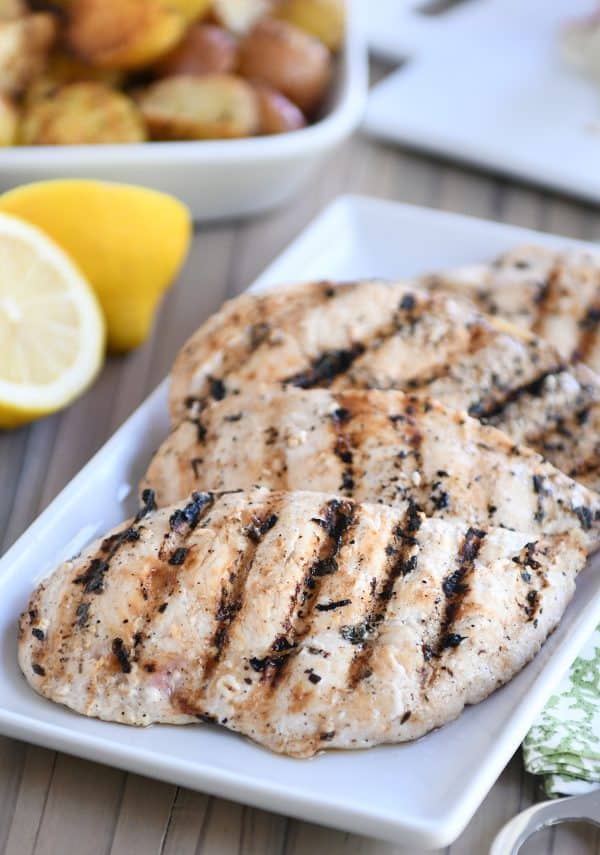 Several lemon garlic grilled chicken breasts on white platter.