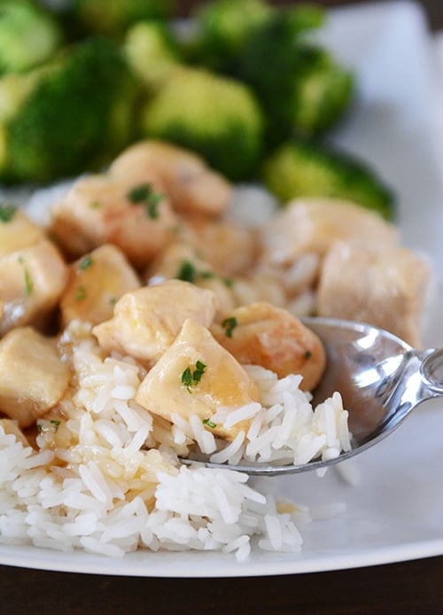 A spoon taking a bite of cooked white rice and lemon-glazed chicken.