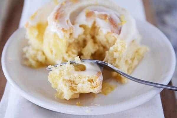 Frosted sticky bun on white plate with fork taking a bite.