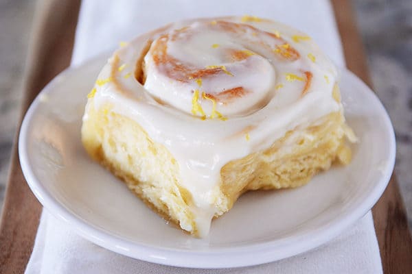 Whole frosted lemon sticky bun on white plate.