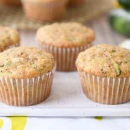 Several lemon poppy seed zucchini muffins on white plate.
