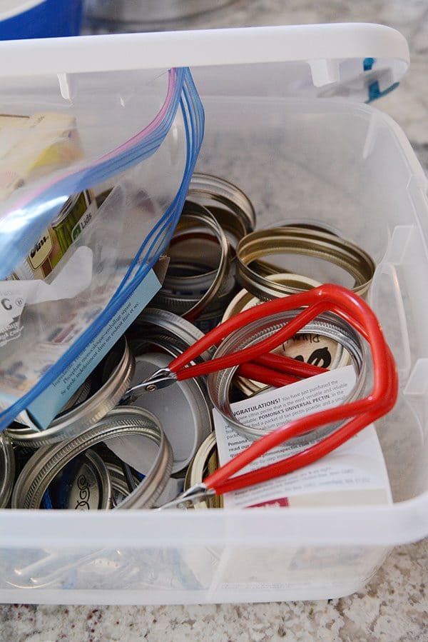 A tupperware of canning lids and supplies.