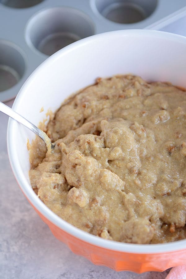 Bran muffin batter in an orange bowl with a spoon on the side. 