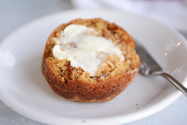 A half of a bran muffin on a white plate with butter spread on it. 