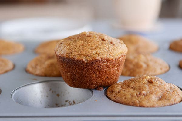 A muffin tin full of cooked bran muffins, with one muffin taken out and placed on top. 