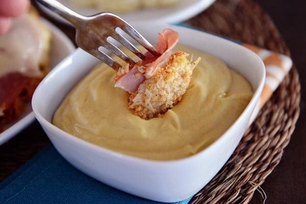 A fork with a bite of chicken and ham getting dipped into a bowl of sauce.