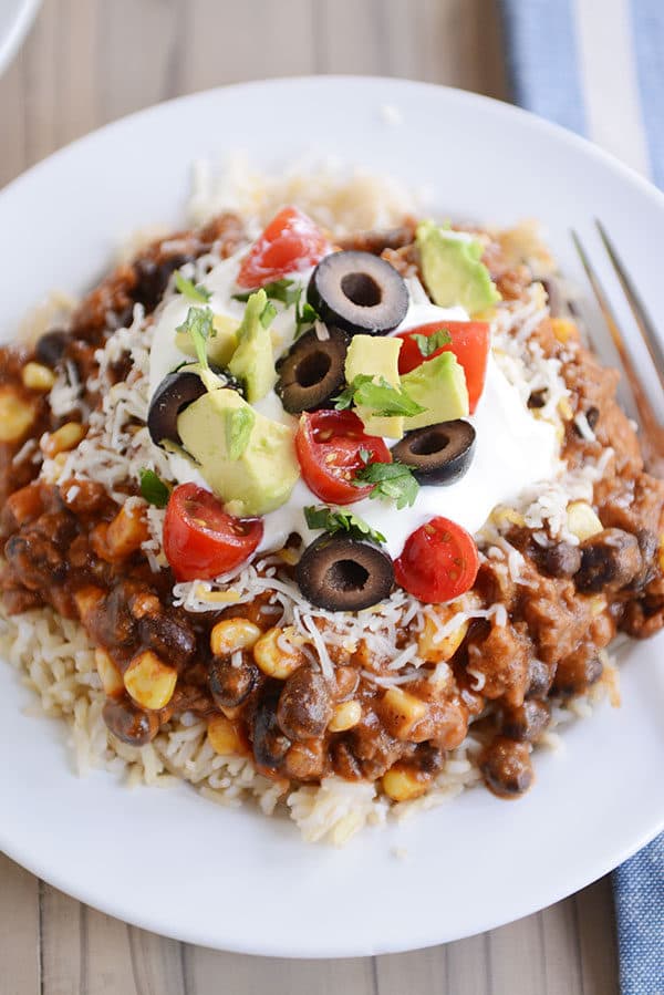 Top view of a white plate of cooked rice topped with a beef and corn mixture and taco toppings.