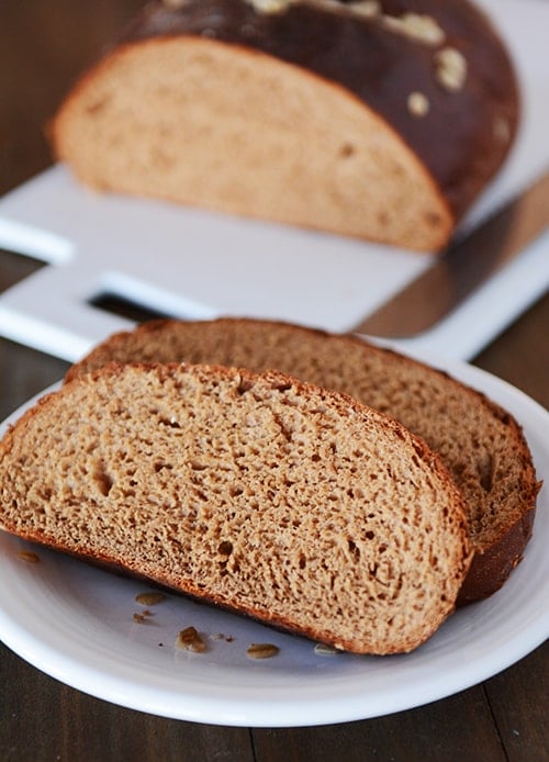 Two slices of dark-colored molasses bread cut off of the loaf, laying on a white plate.