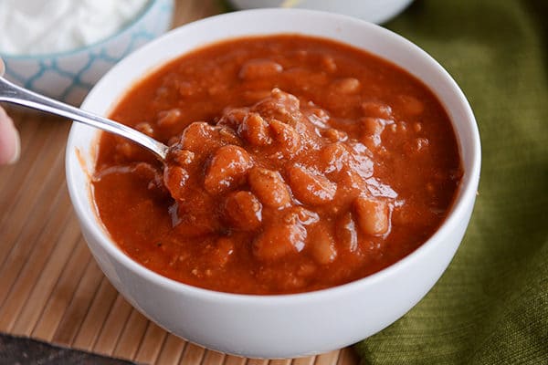 A white bowl full of red chili with a spoon in it.