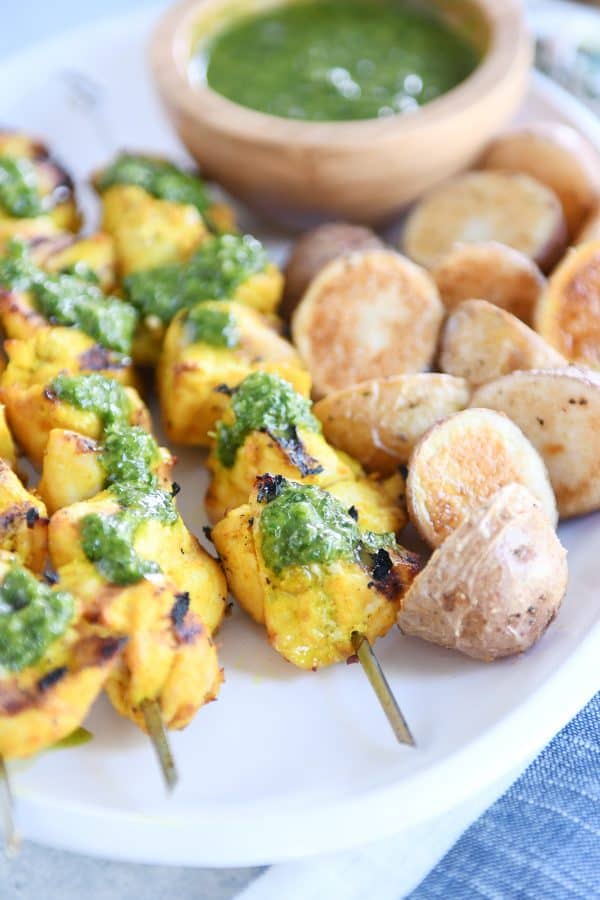 Close up view of green sauce on Moroccan chicken skewer with a couple roasted potatoes.