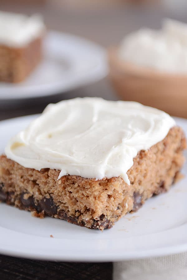 A piece of frosted oatmeal chocolate chip cake on a white plate.