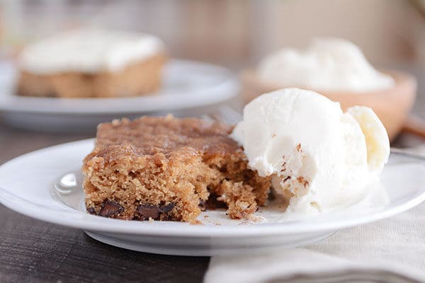 A piece of oatmeal chocolate chip cake next to a scoop of vanilla ice cream.
