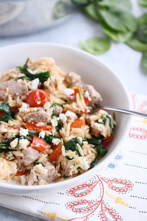 White bowl filled with orzo, spinach, bell peppers and pork.