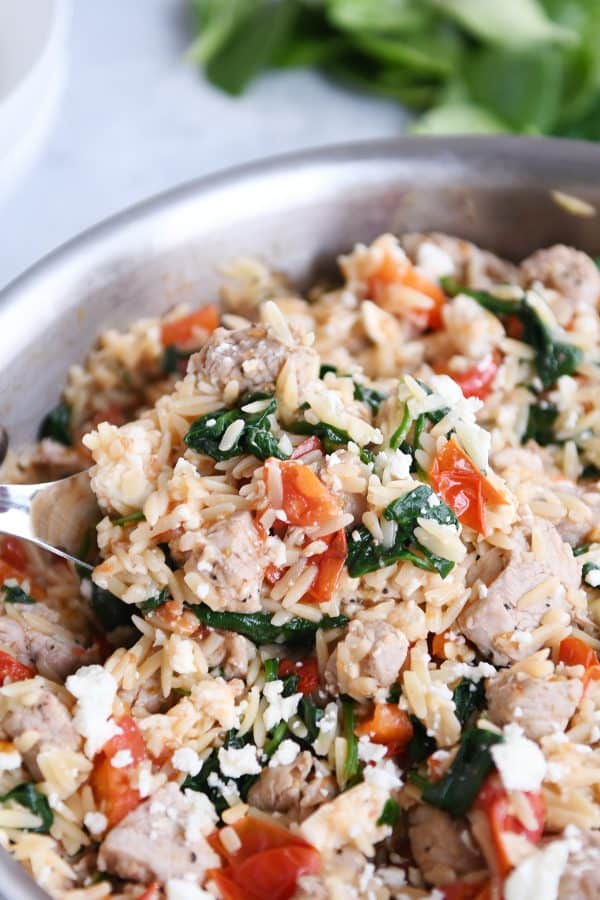 Mediterranean orzo skillet with serving spoon.