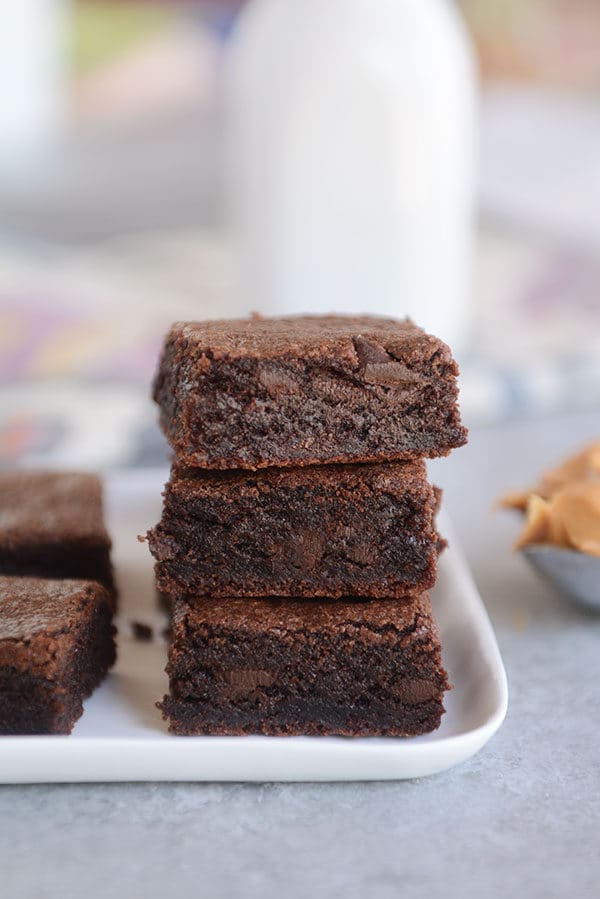 Three chocolate brownies stacked on top of each other on a white plate.