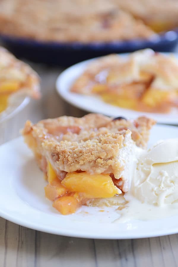 A slice of peach pie with a bite taken out next to a scoop of vanilla ice cream on a white plate.
