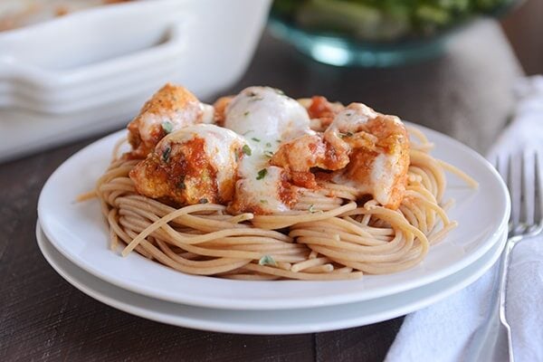 A plate of spaghetti topped with pesto marinara cheesy chicken.