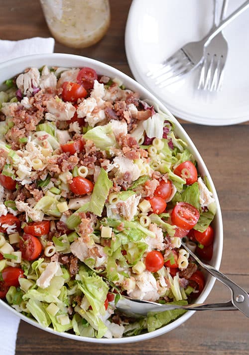 A large oval bowl full of Portillo's chopped salad with bacon, tomatoes, and chicken on top.
