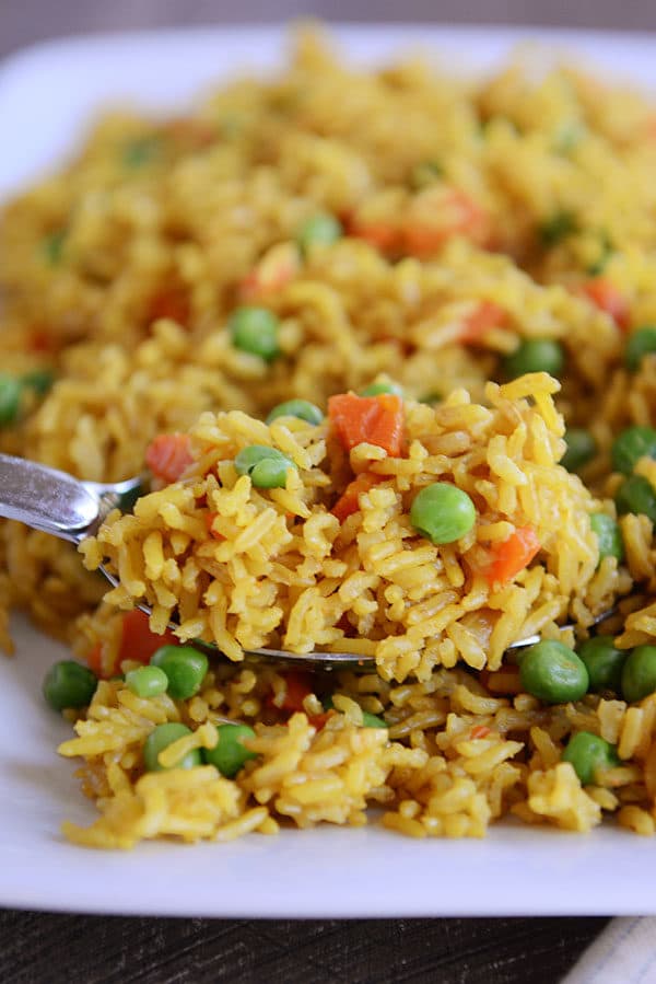 A spoon with a big scoop of yellow-tinted rice and peas and carrots sprinkled throughout. 