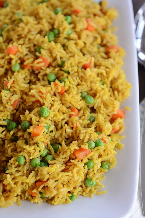 A white platter full of yellow-tinted rice with peas and carrots throughout. 