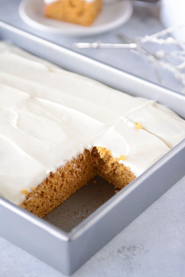 A metal pan of frosted pumpkin bars with two pieces already cut out.