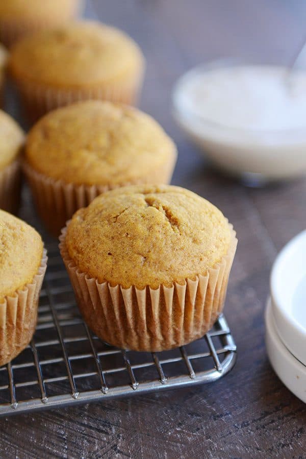 Pumpkin muffins on a cooling rack with a bowl of frosting on the side.