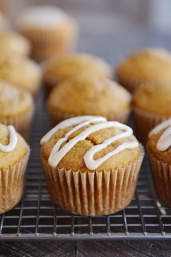 Pumpkin muffins with a drizzle of syrup on the front muffins, all sitting on a cooling rack.