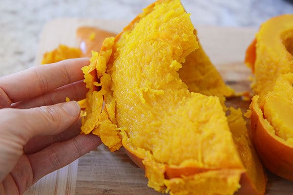 A hand pulling the skin off of a chunk of cooked pumpkin.